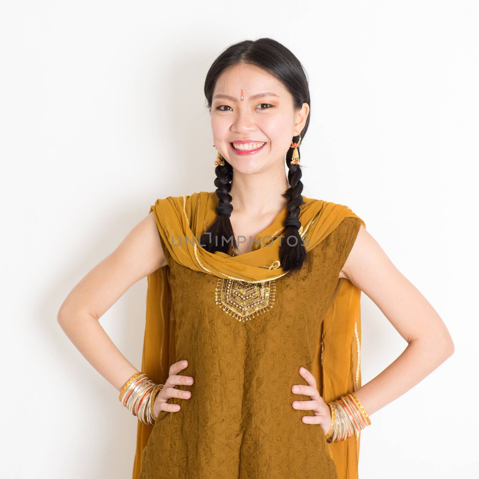 Portrait of beautiful mixed race Indian Chinese woman in traditional Punjabi dress smiling, standing on plain white background.