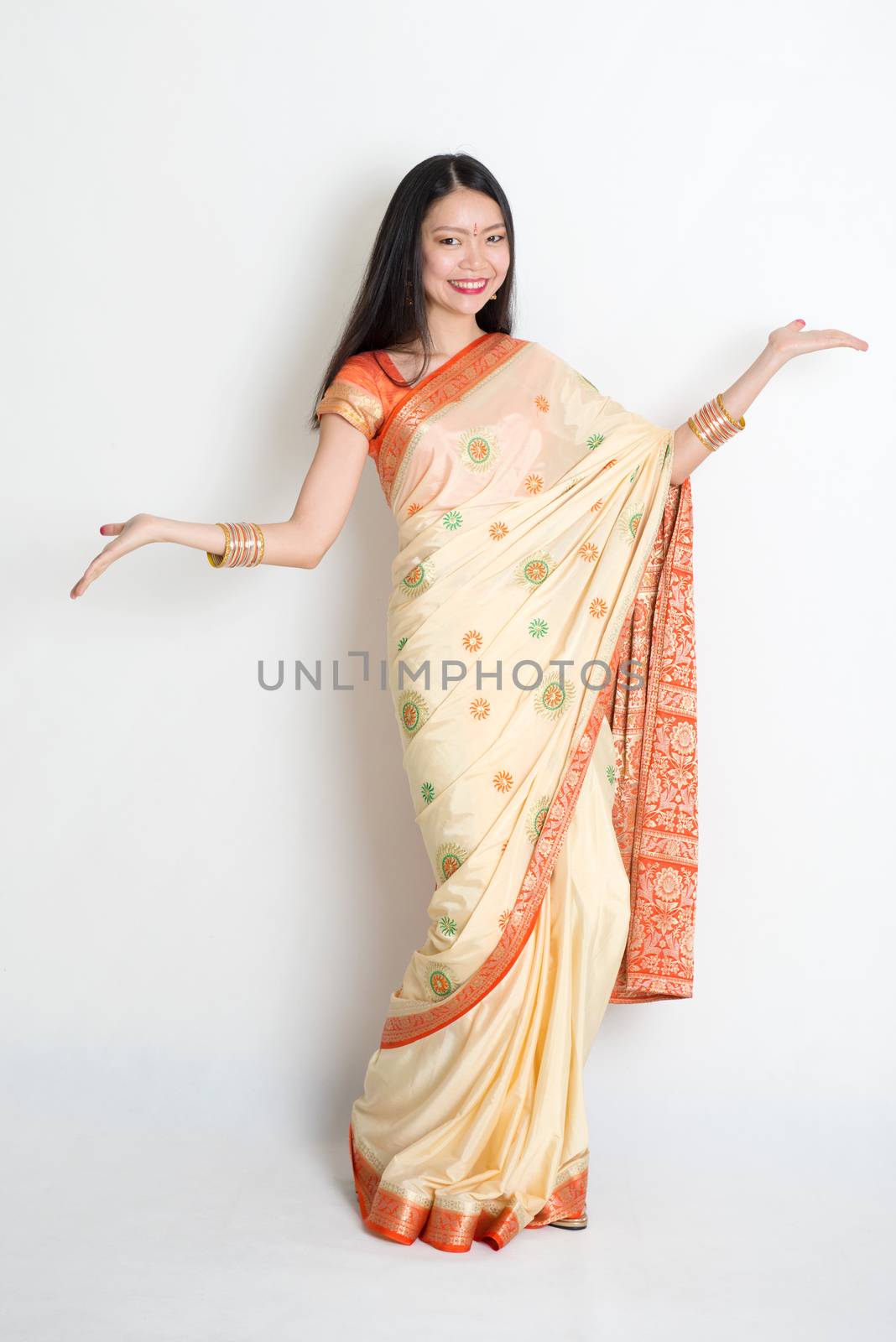 Portrait of young mixed race Indian Chinese woman in traditional sari dress dancing, on plain background.