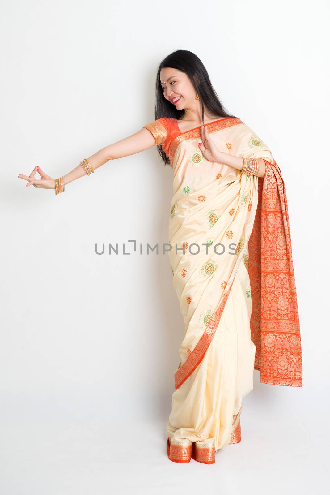 Portrait of young mixed race Indian Chinese woman in traditional sari dress dancing, full length on plain background.