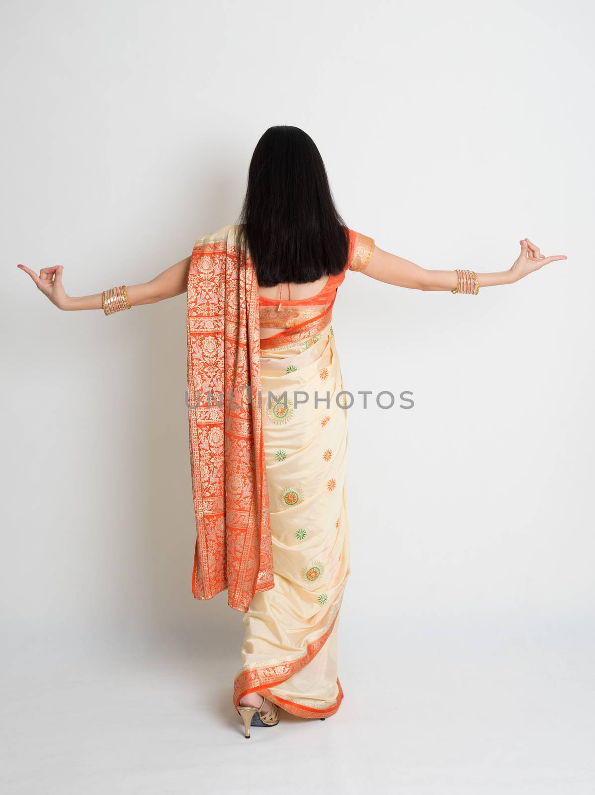 Rear view of young mixed race Indian Chinese woman in traditional sari dress dancing, full length on plain background.
