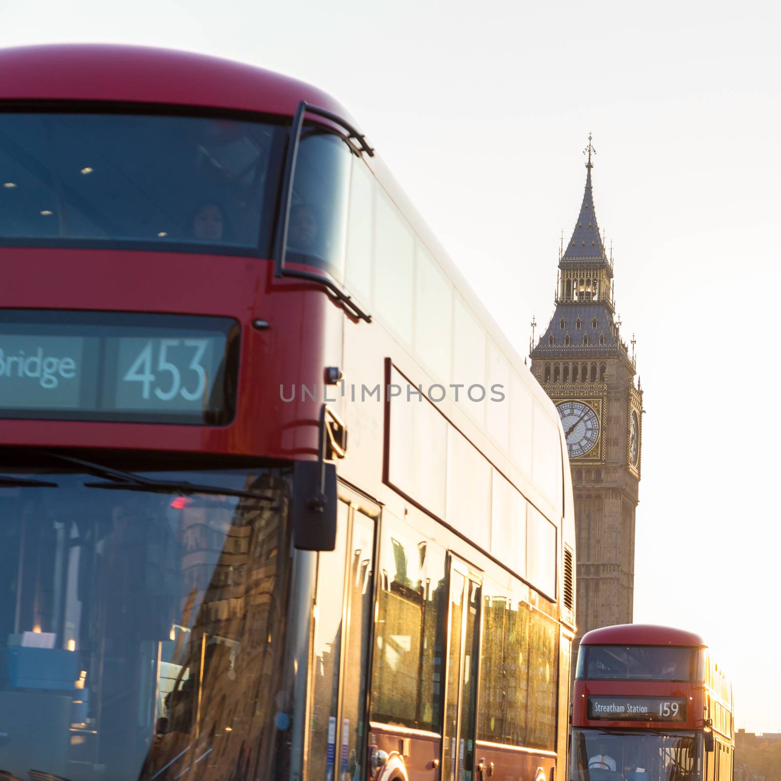 Traditionally red double-decker buses passing on Westminster Bridge in sunset in London, UK. Big ben and Palace of Westminster aka Houses of Parliament in background.