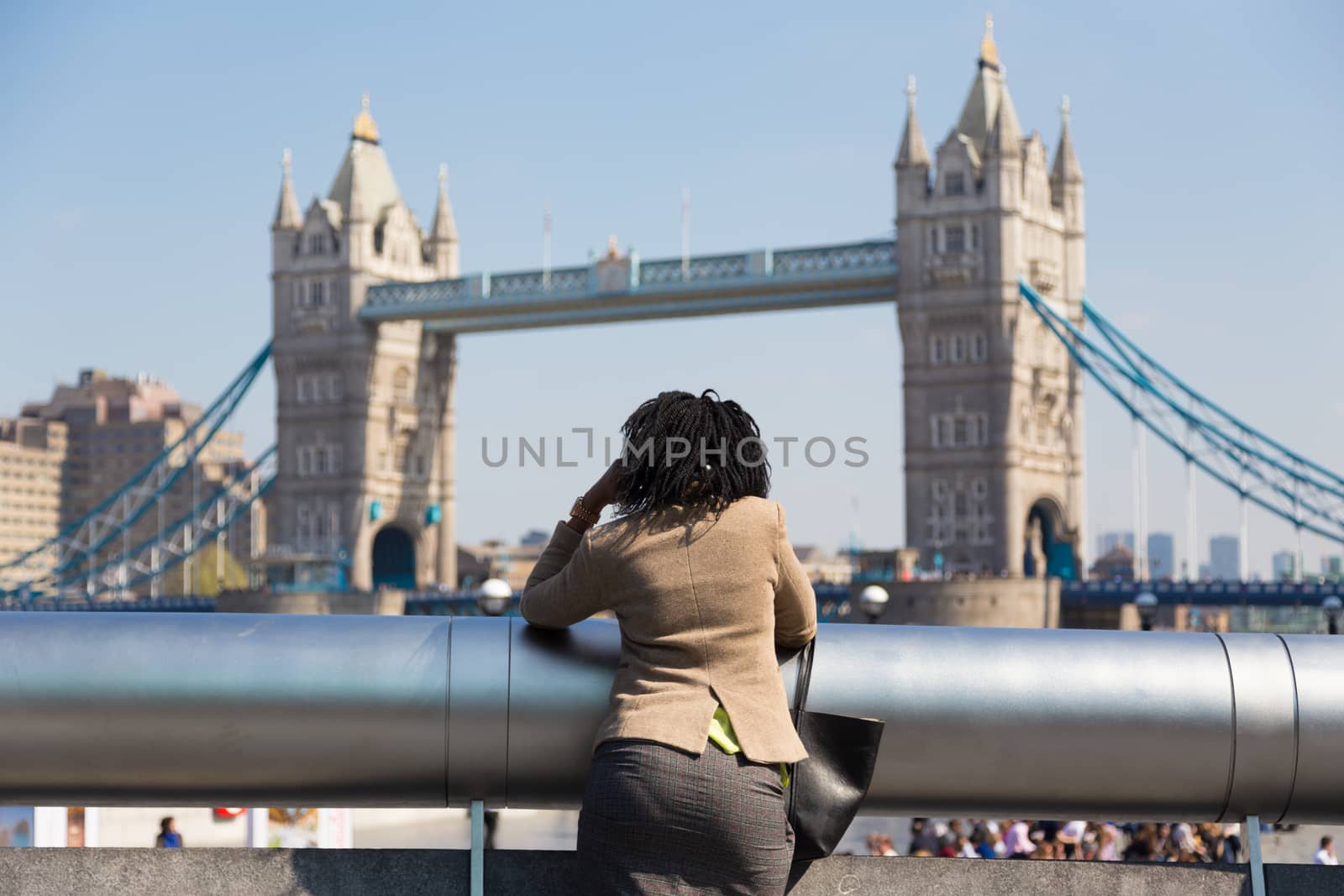 Businesswoman talking on mobile phone outdoor, looking at Tower Bridge in London city, UK.
