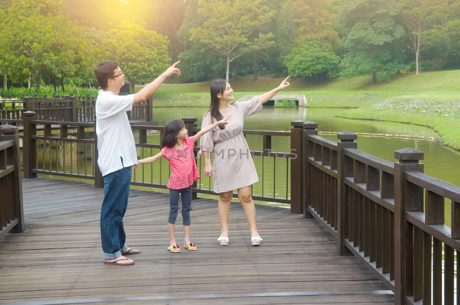 Happy Asian family pointing away, outdoor lifestyle at nature green park.