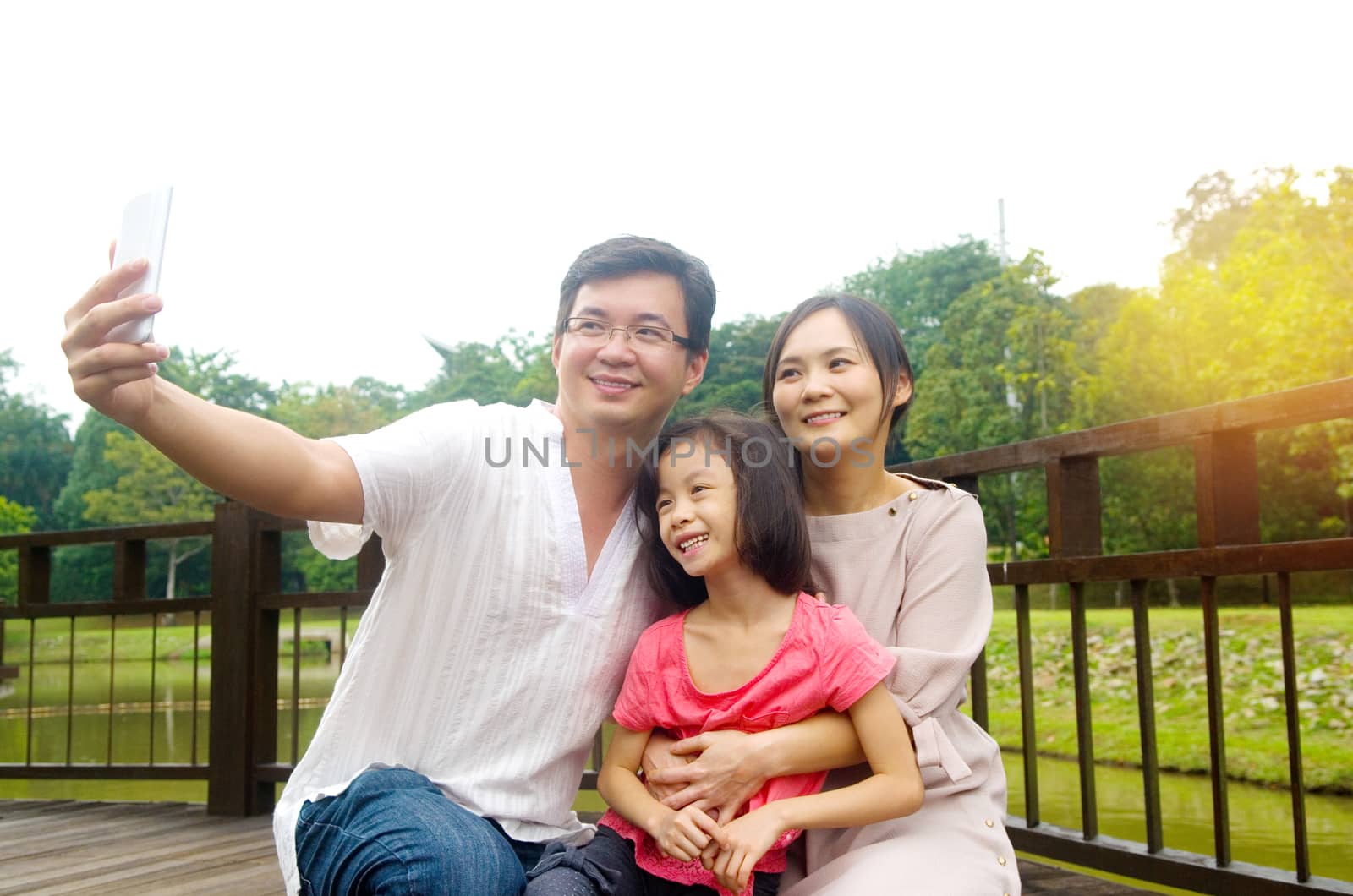 happy asian family taking a outdoor selfie in a city park.