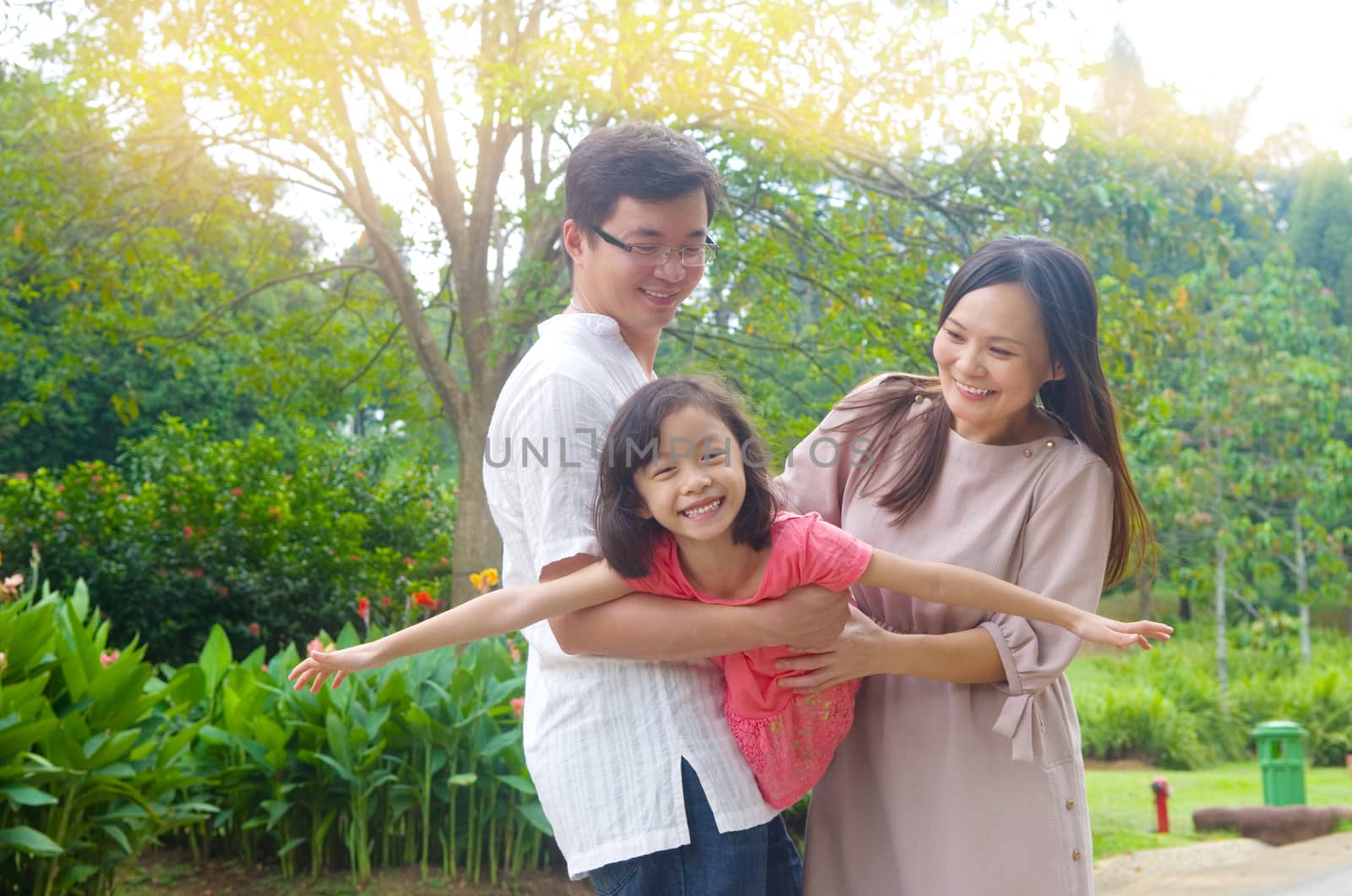 Portrait of joyful happy Asian family playing together at outdoor park during summer sunset.