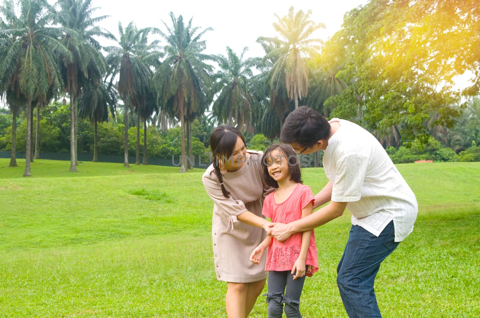 Portrait of joyful happy Asian family playing together at outdoor park during summer sunset.