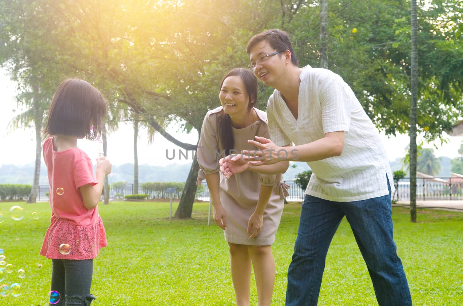 Portrait of joyful happy Asian family playing bubbles together at outdoor park during summer sunset.