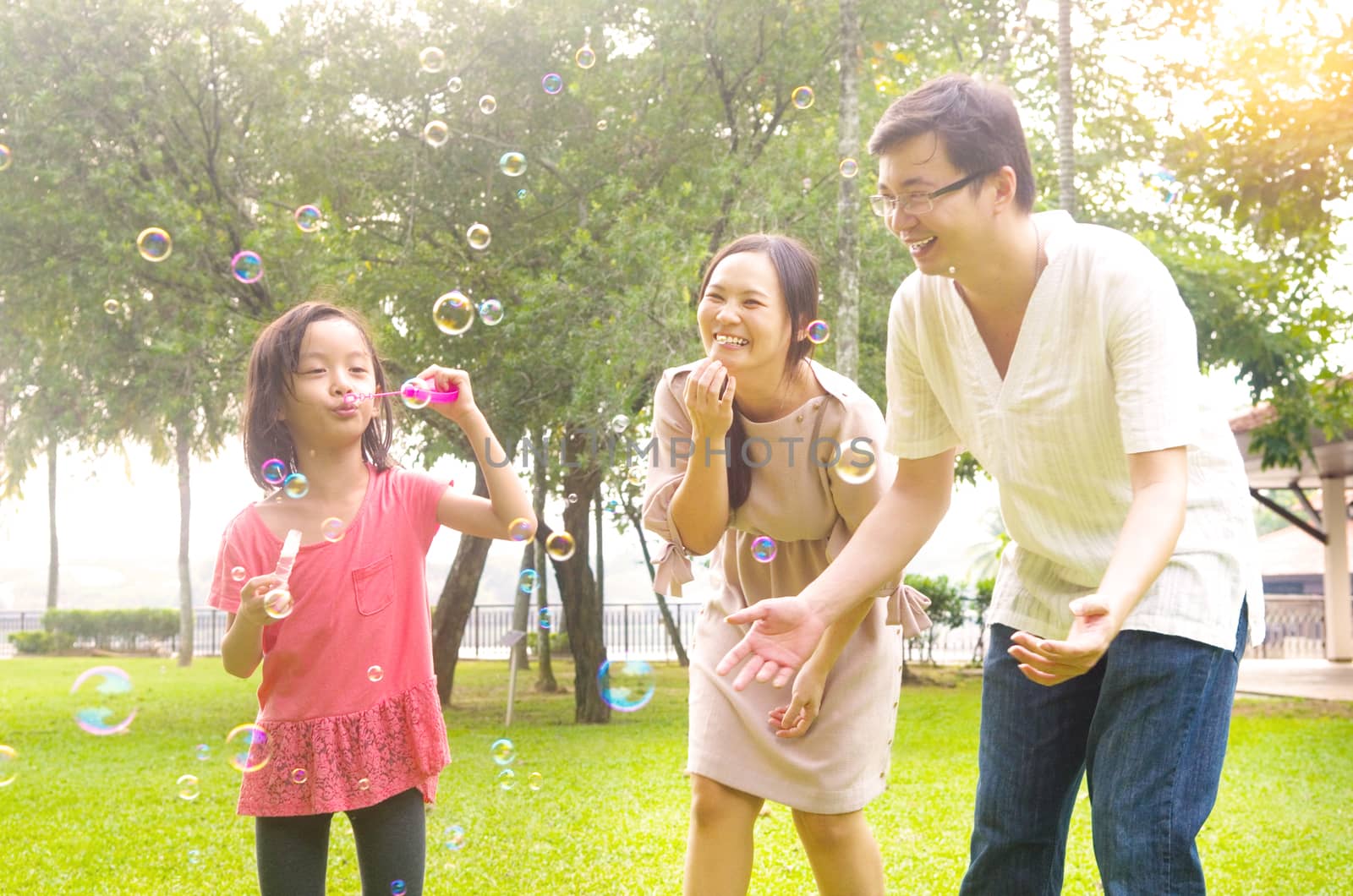 Portrait of joyful happy Asian family playing bubbles together at outdoor park during summer sunset.