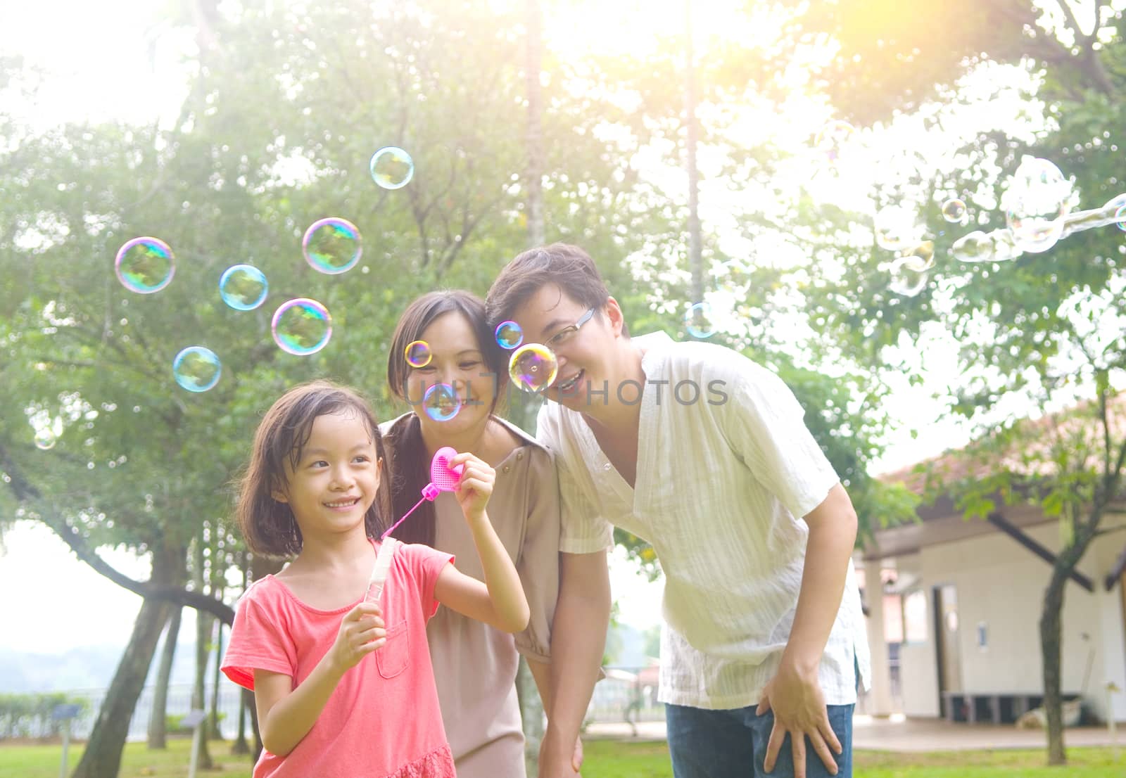 Portrait of joyful happy Asian family playing bubbles together at outdoor park during summer sunset.