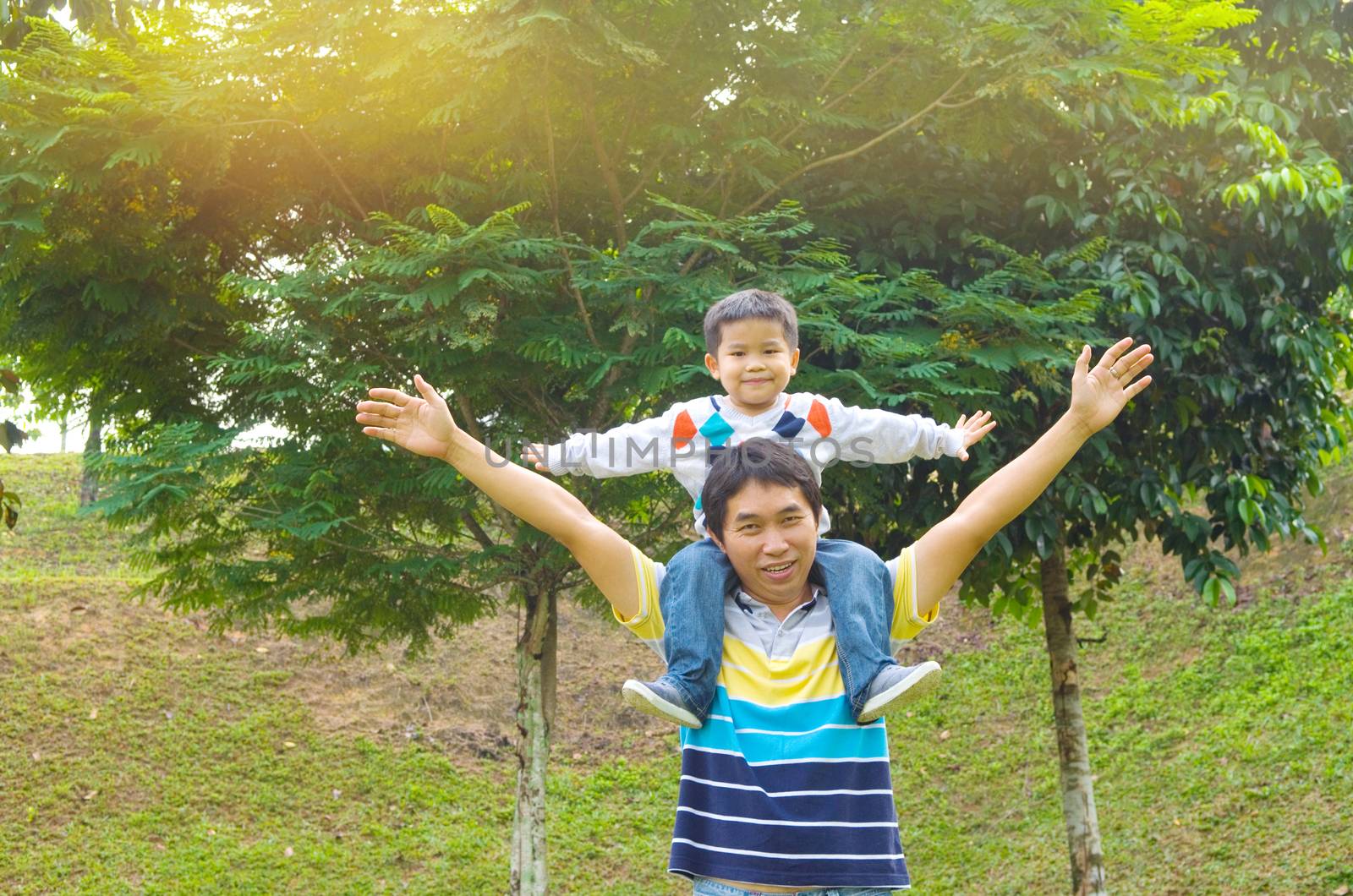 Asian father giving piggyback ride to his son in the evening sunshine