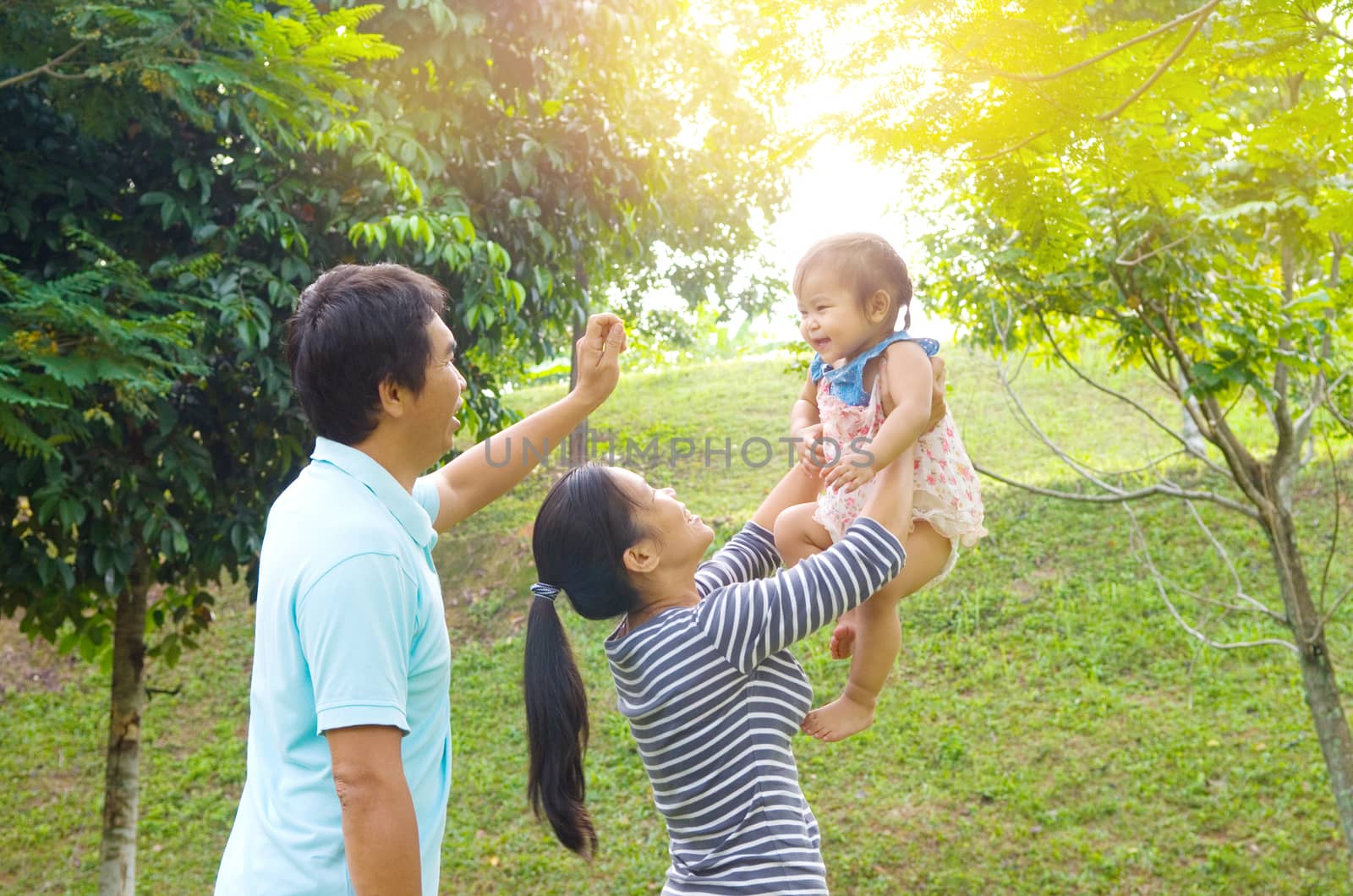 Happy Asian family playing in park during summer sunset, outdoors shot.