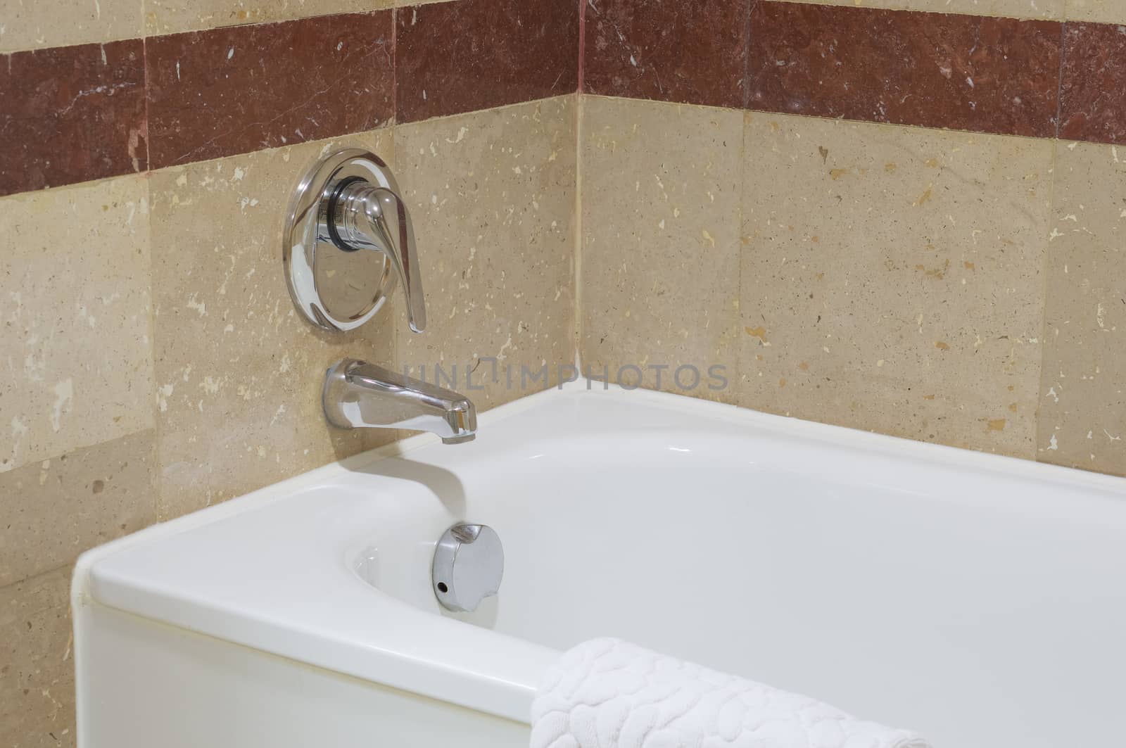 Close up white luxury bathtub with chrome faucet on brown tile wall.