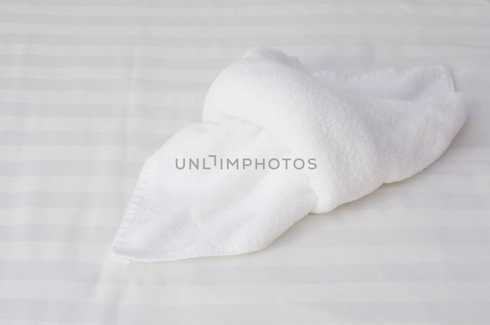 Close up white towel fold on white bed in hotel room.