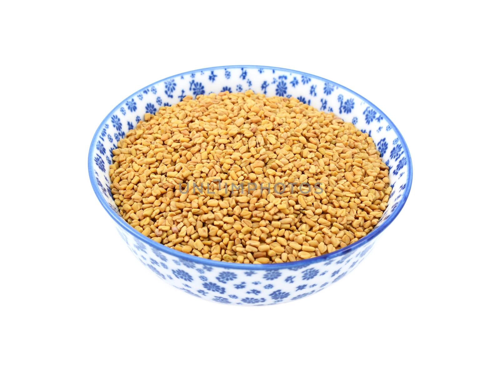 Fenugreek seeds in a blue and white porcelain bowl with a floral design, isolated on a white background