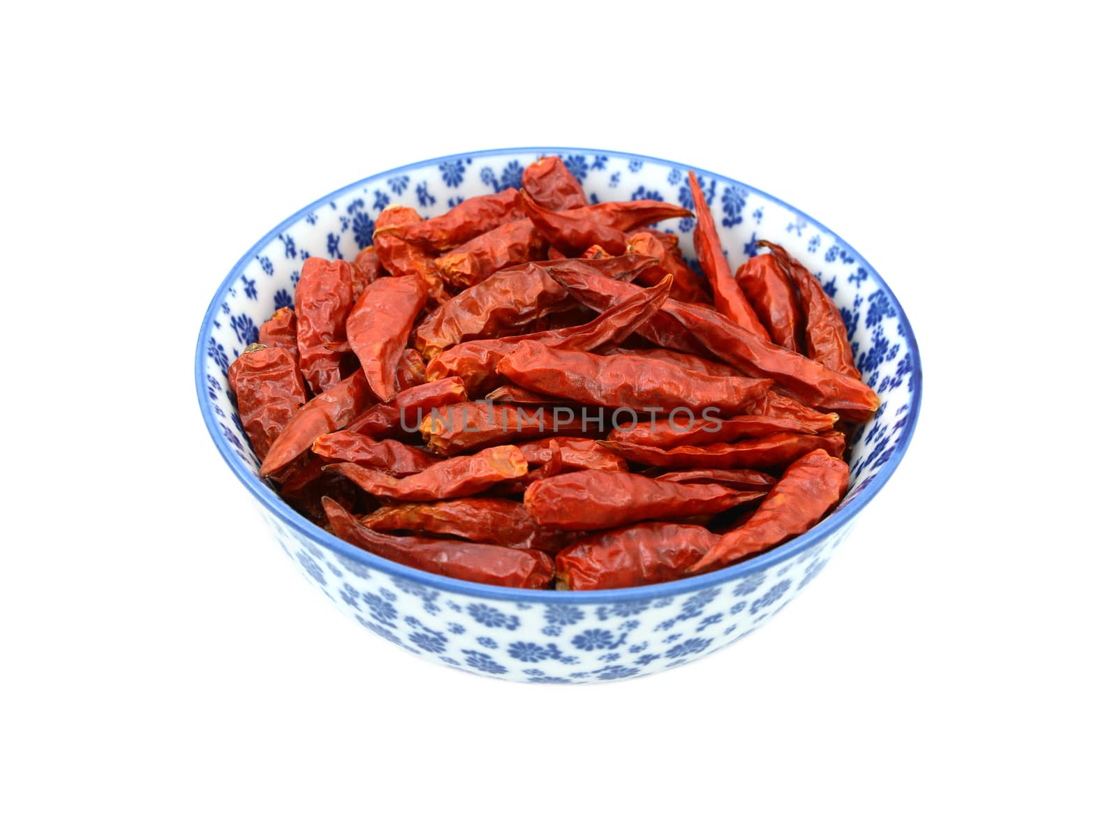 Birds eye chillis in a blue and white porcelain bowl with a floral design, isolated on a white background