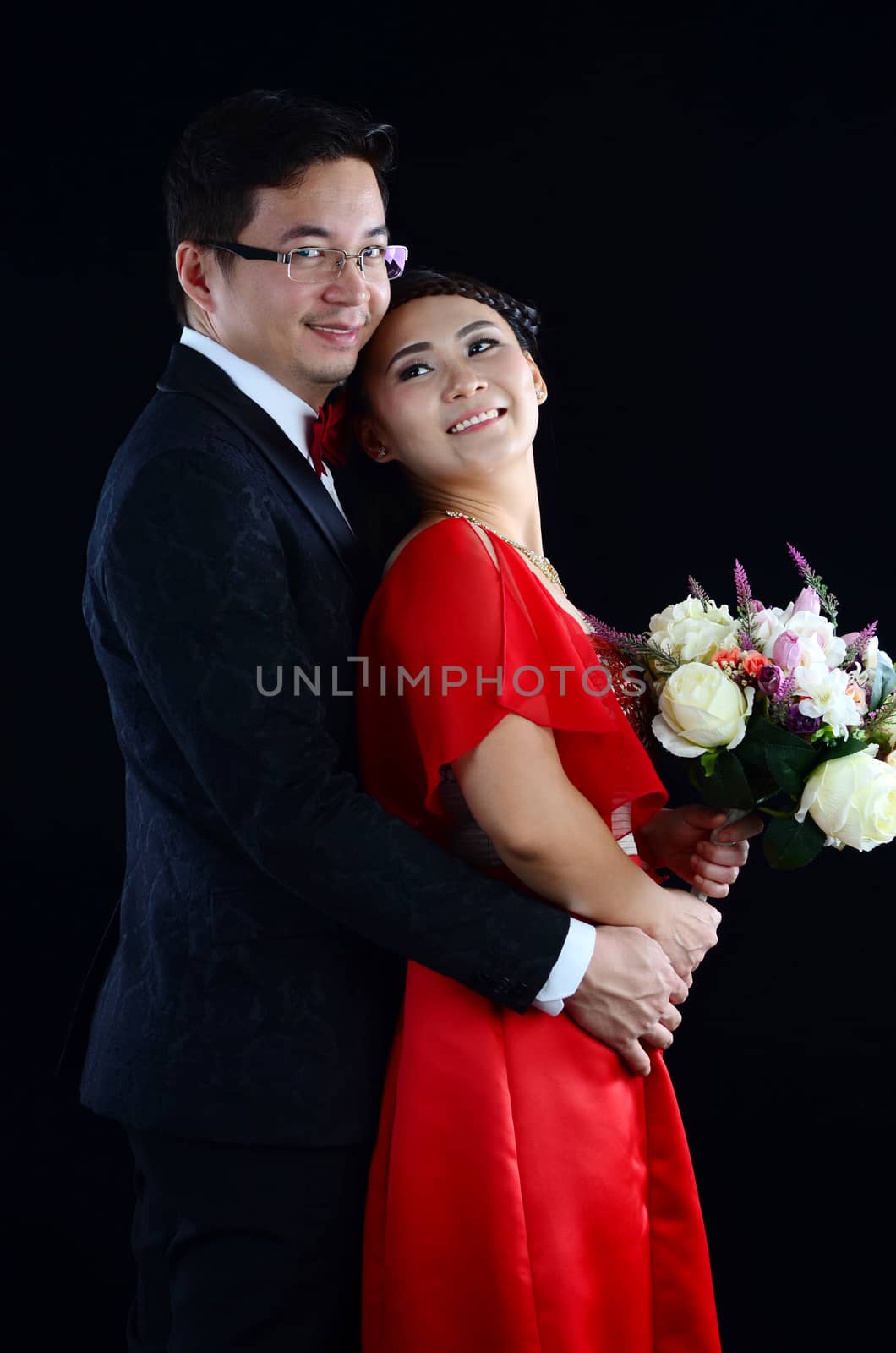 Portrait of young elegant enamoured just married groom and bride embracing at Wedding on black background