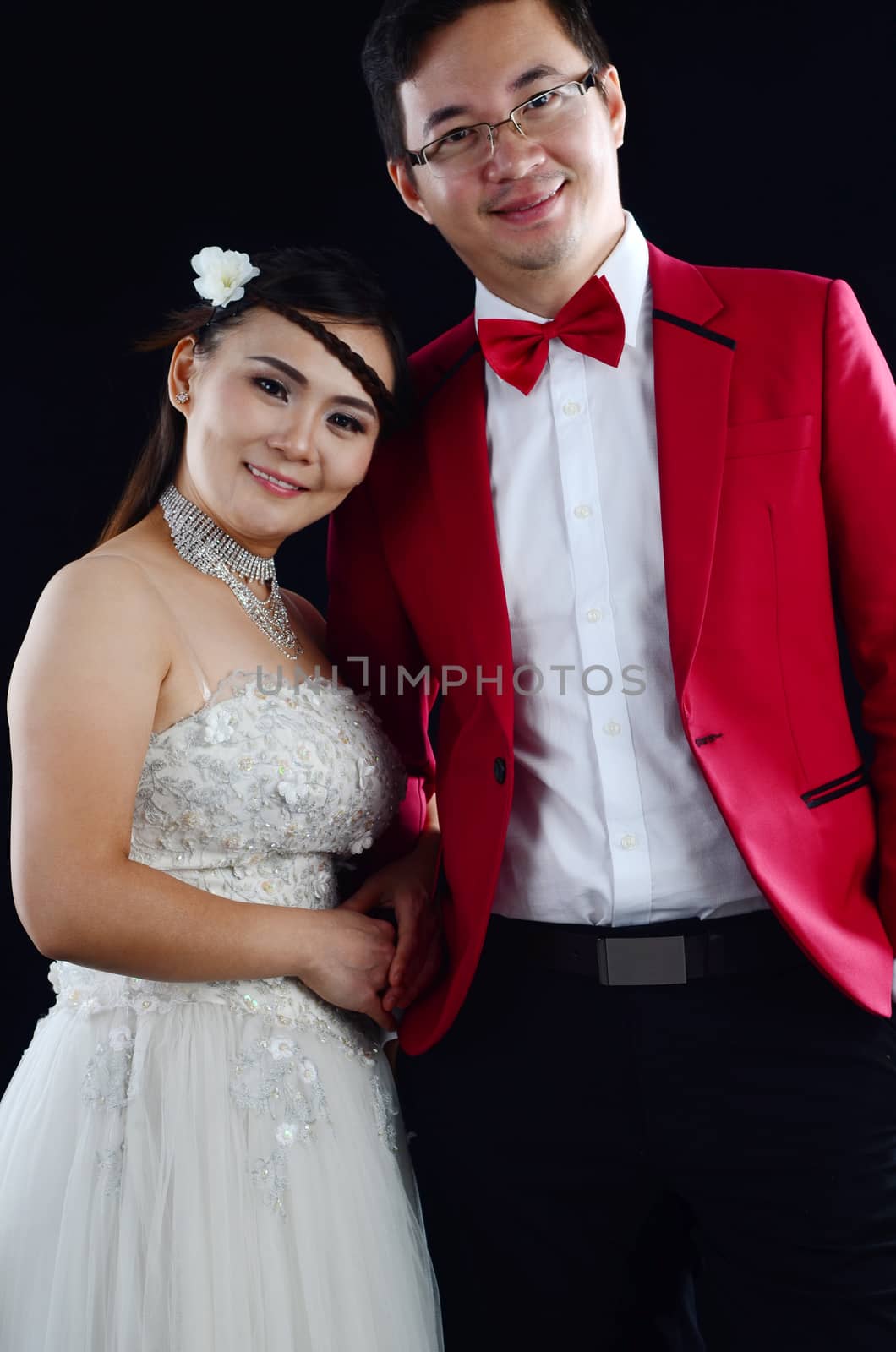 Portrait of young elegant enamoured just married groom and bride embracing at Wedding on black background