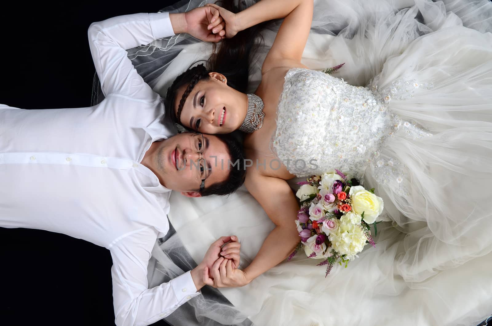 Portrait of young elegant enamoured just married groom and bride embracing at Wedding on black background