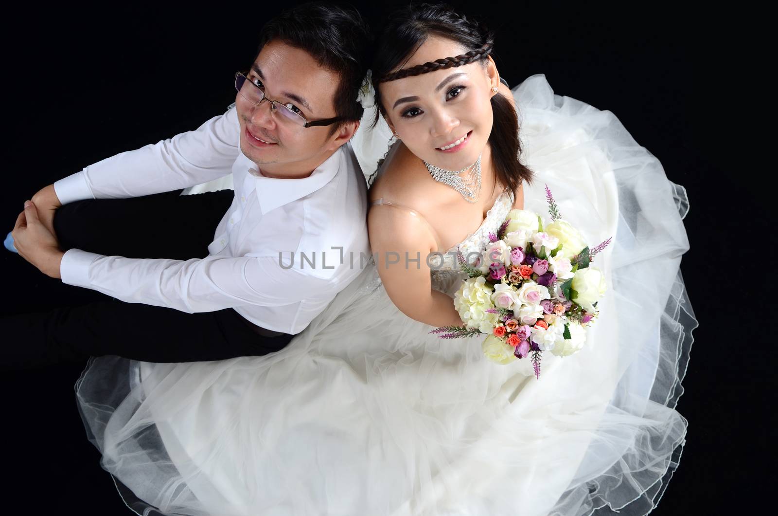 Portrait of young elegant enamoured just married groom and bride embracing at Wedding on black background