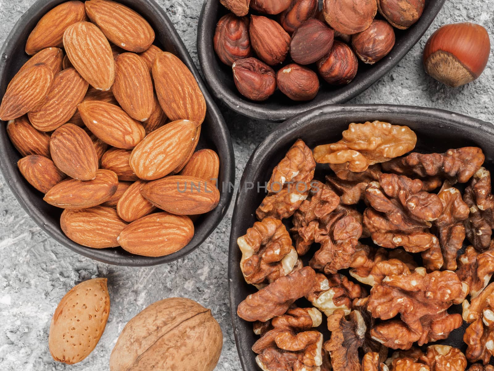 Walnuts, almonds and hazelnuts in trendy plates on gray cement background. Top view or flat lay.