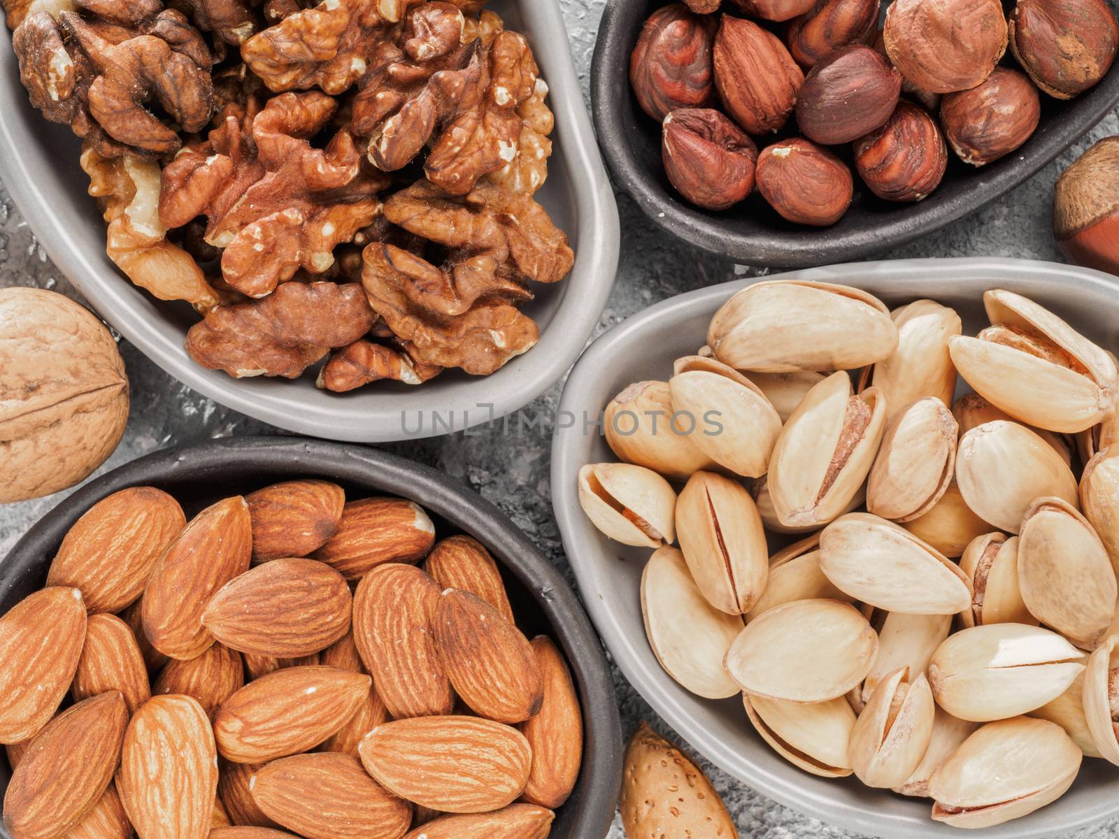 Walnuts, almonds, pistachios and hazelnuts in trendy plates on gray cement background. Top view or flat lay.