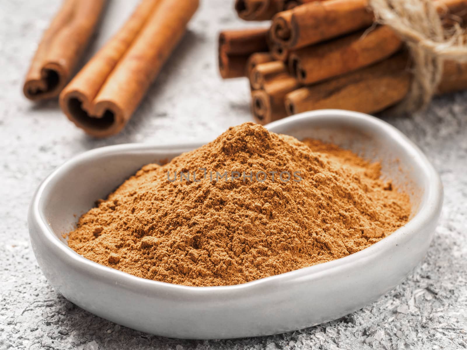 Close up view of ground cinnamon in trendy plate and cinnamon sticks on gray cement background