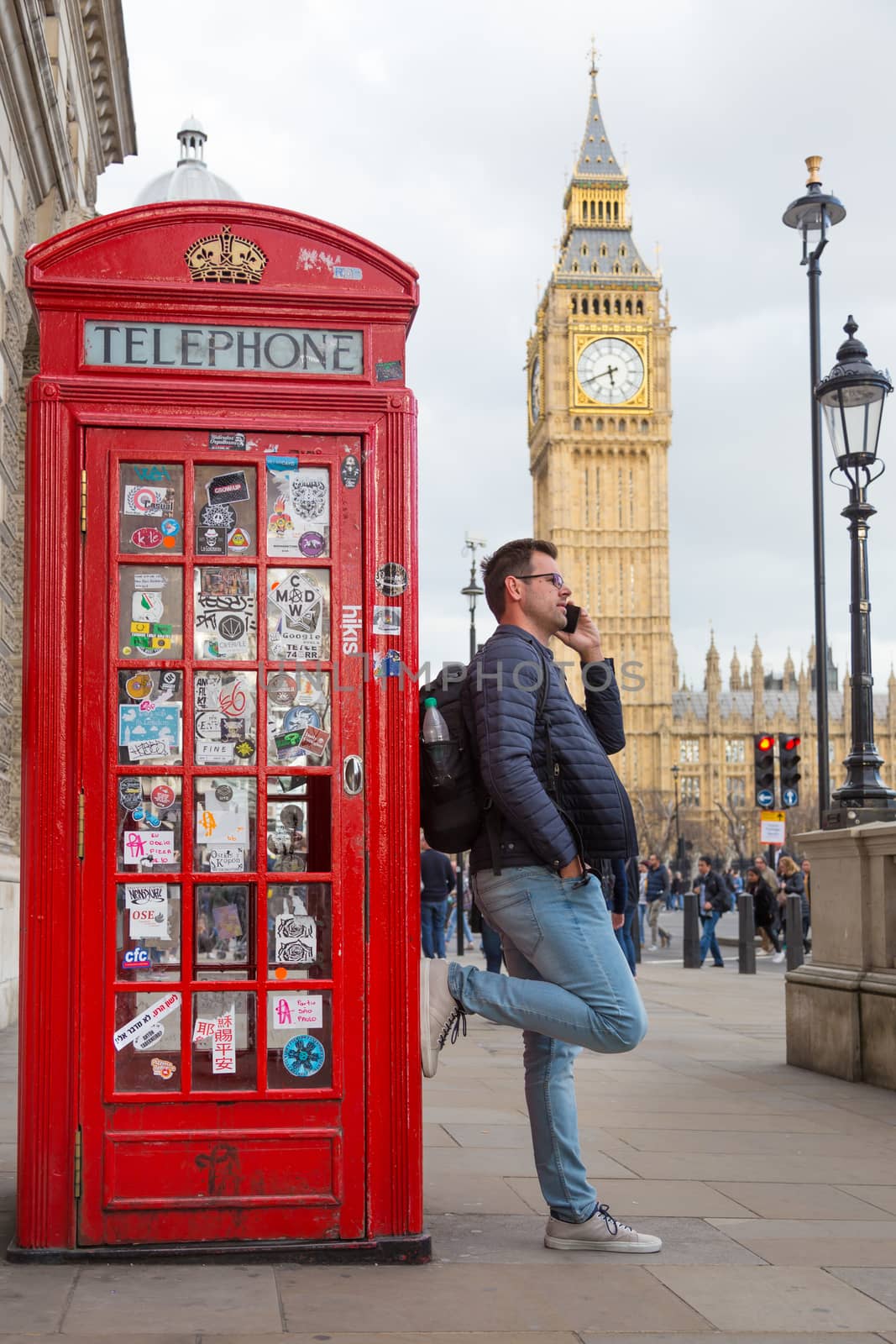 Casual man talking on mobile phone in London, leaning on traditional british red telephone booth. Big Ben can be seen in background. London, England.