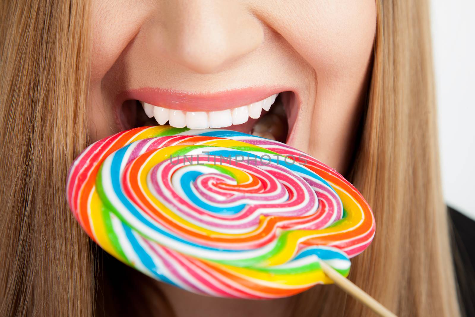 A close-up of a female mouth wide open going to take a bite of a big colorful spiral lollipop.