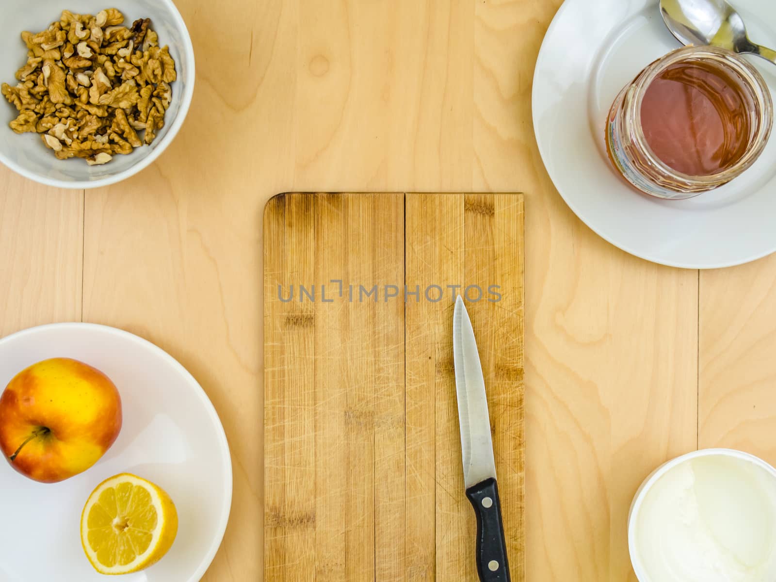 Four ingredients for a healthy and nutritious snack or smoothie, around board and knife, apple lemon fruit, cottage cheese, honey , shelled nuts walnuts, on plates from top view, arranged on wooden table in soft colours with copy space in the middle
