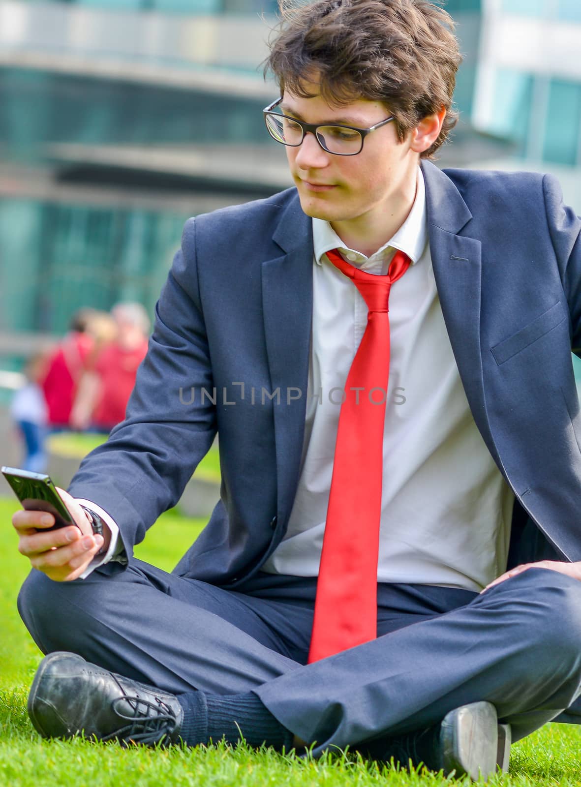 young businessman sitting on the grass, consulting his phone during a break