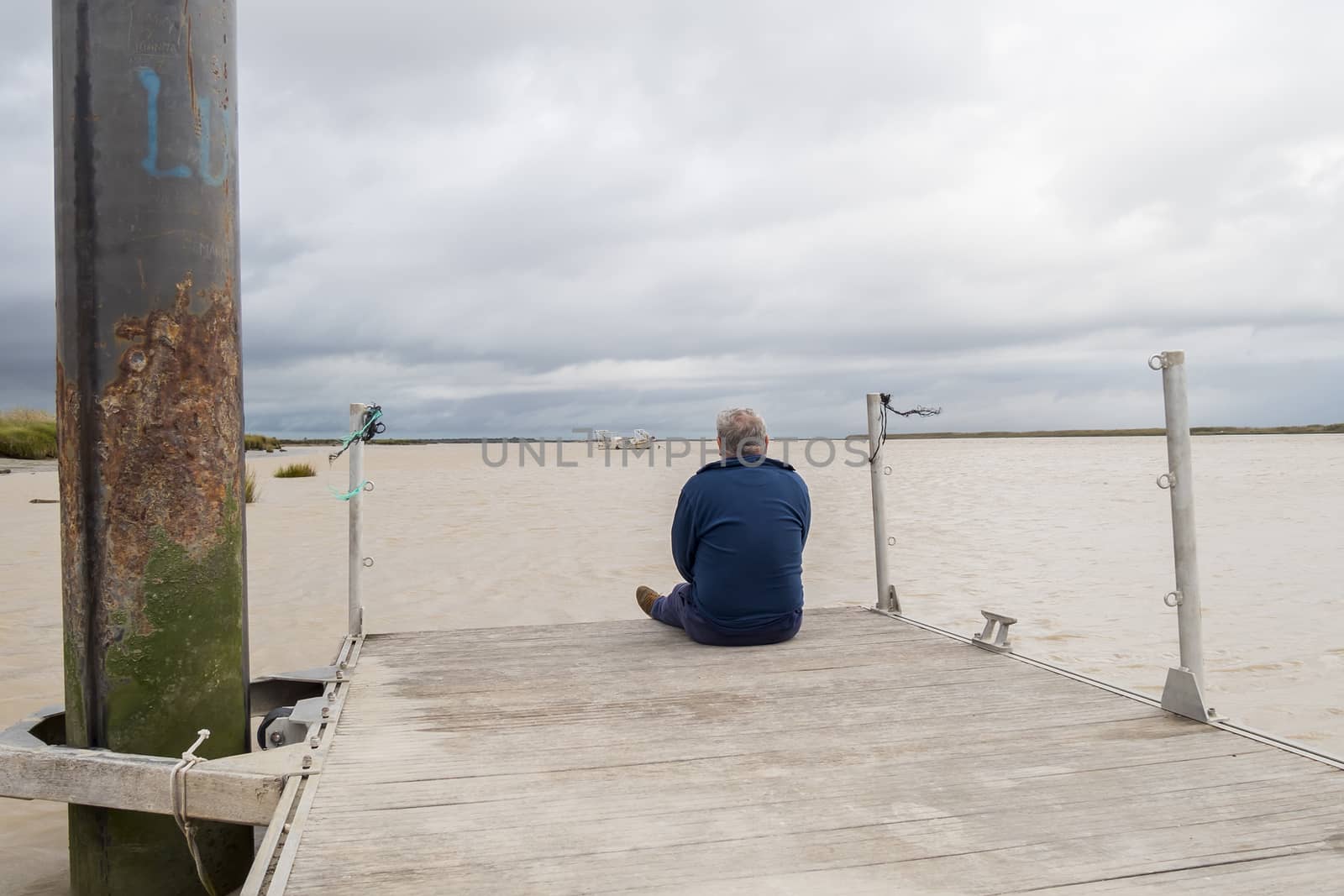 Man sitting on wooden pier facing the river thinking by max8xam