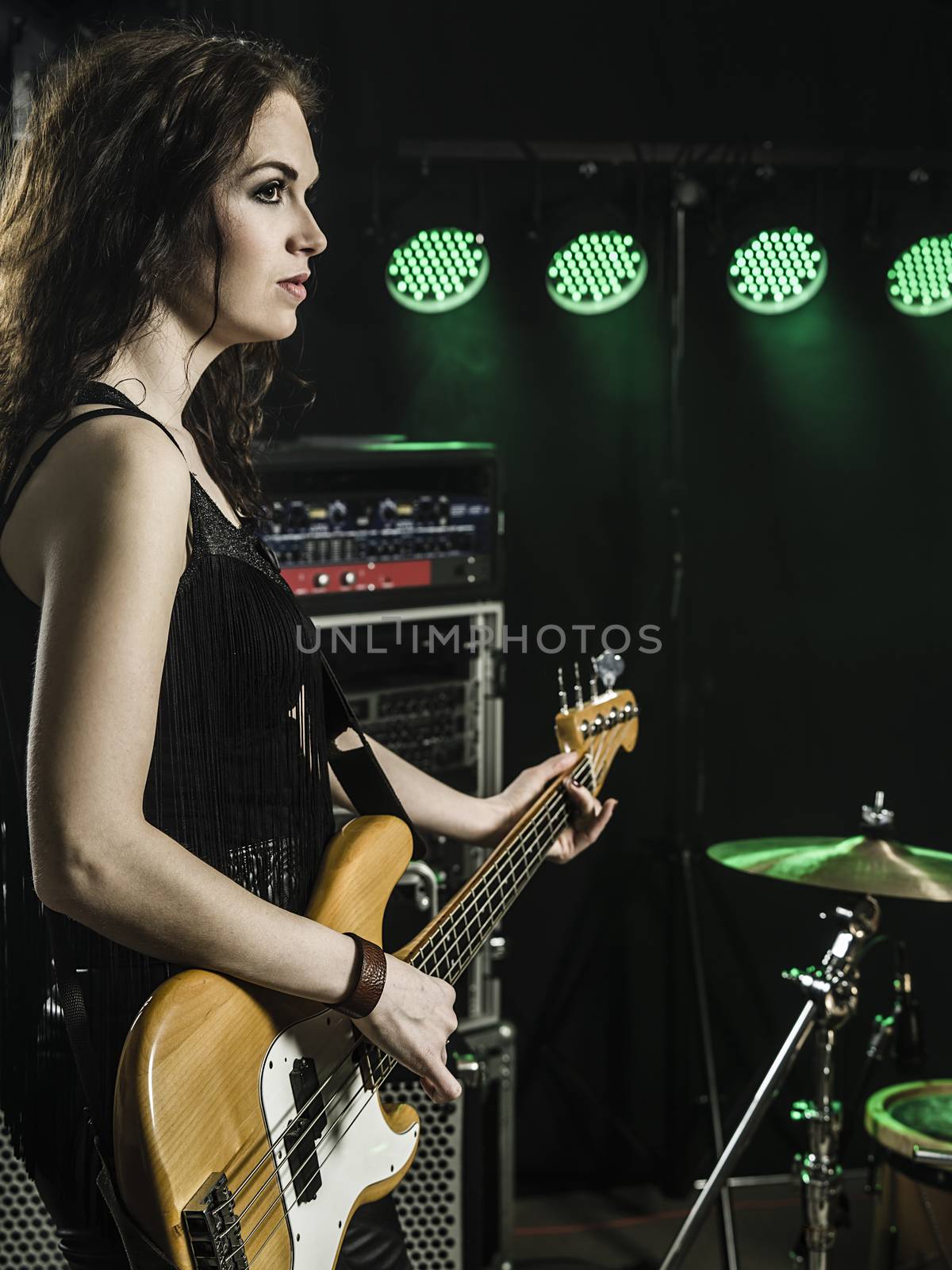 Photo of a beautiful young bass player standing on stage with her guitar.