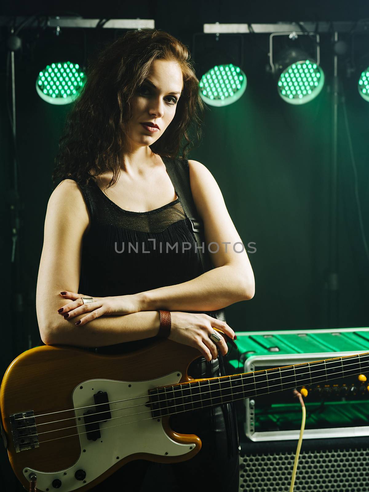 Photo of a beautiful young bass player standing on stage with her guitar.
