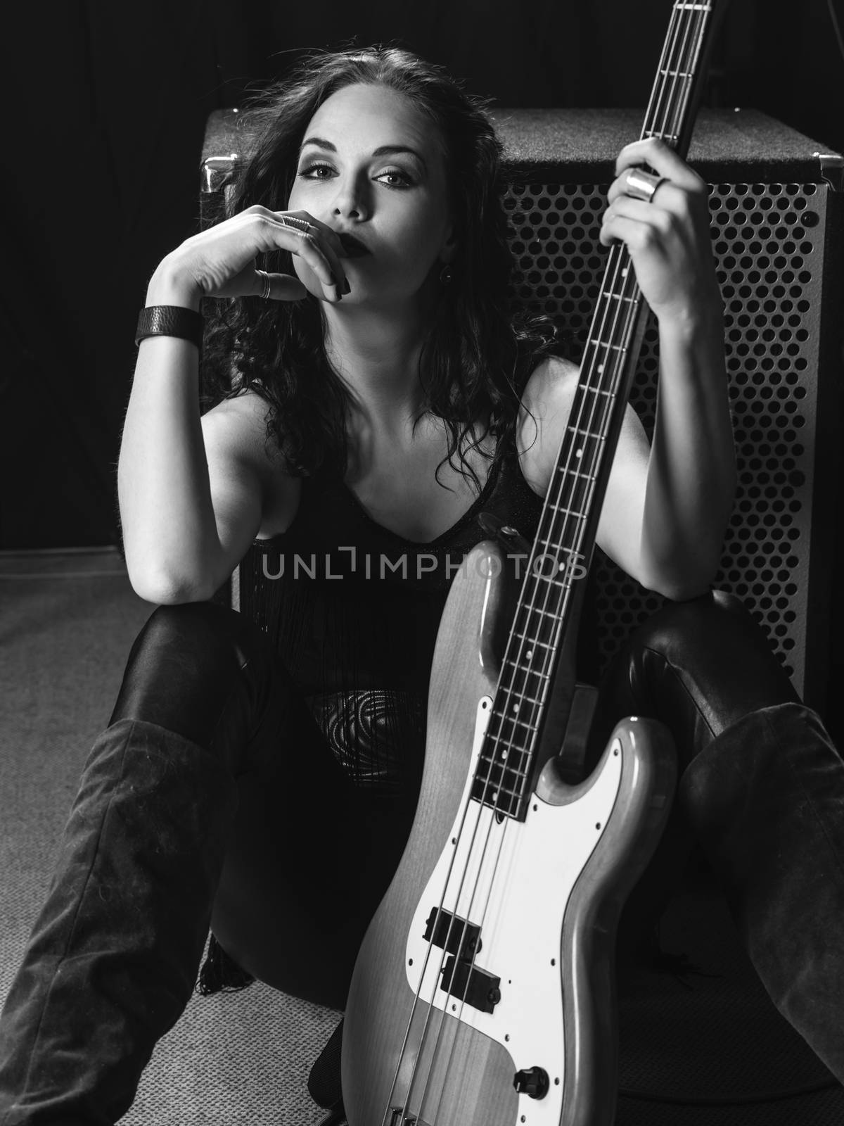 Photo of a beautiful young bass player sitting with her guitar against an amplifier.
