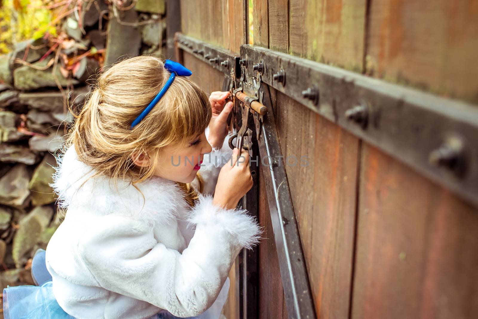 Side view of an little beautiful girl in the scenery of Alice in Wonderland looking into the keyhole of the gate by okskukuruza