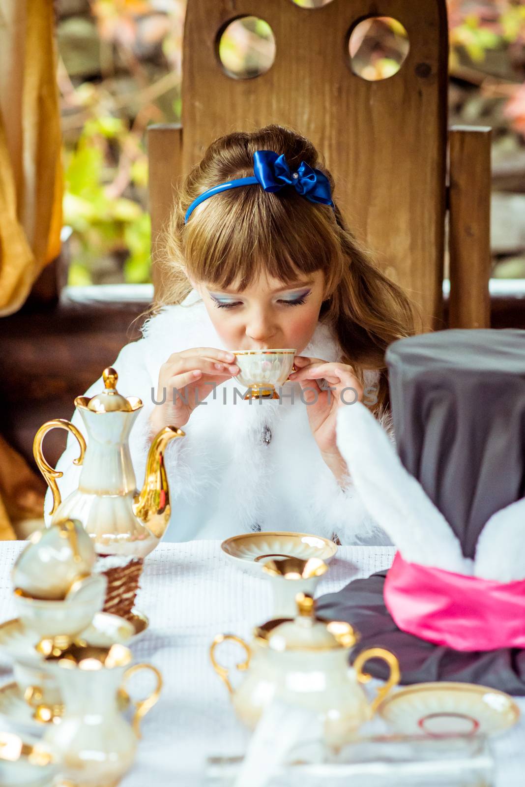 Front view of an little beautiful girl in the scenery of Alice in Wonderland drinking a tea at the table in the park by okskukuruza