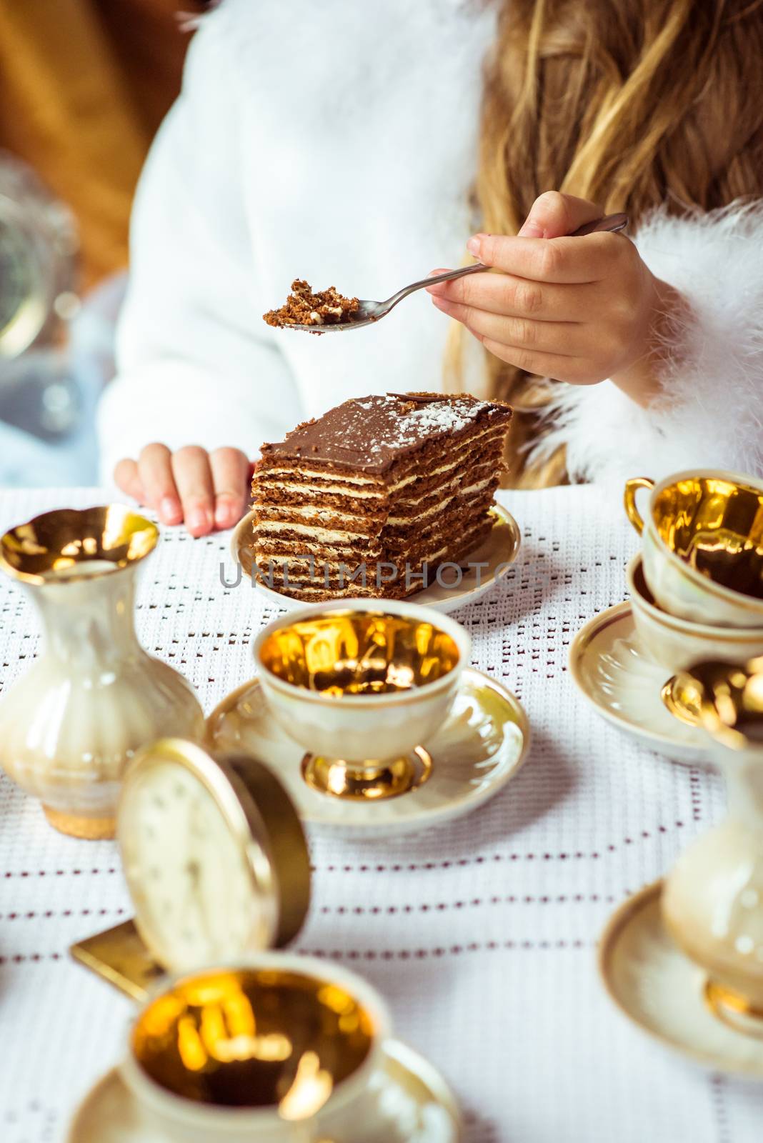 Front view of little beautiful girl's hands in the scenery of Alice in Wonderland holding a piece of cake on a spoon at the table in the autumn park.