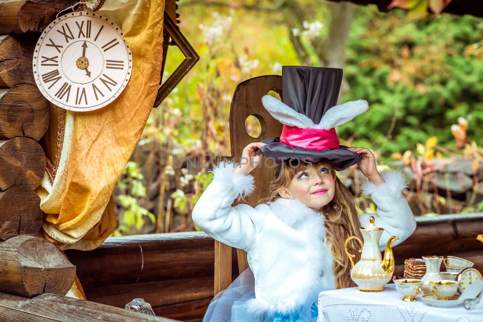 An little beautiful girl holding cylinder hat with ears like a rabbit over head at the table by okskukuruza