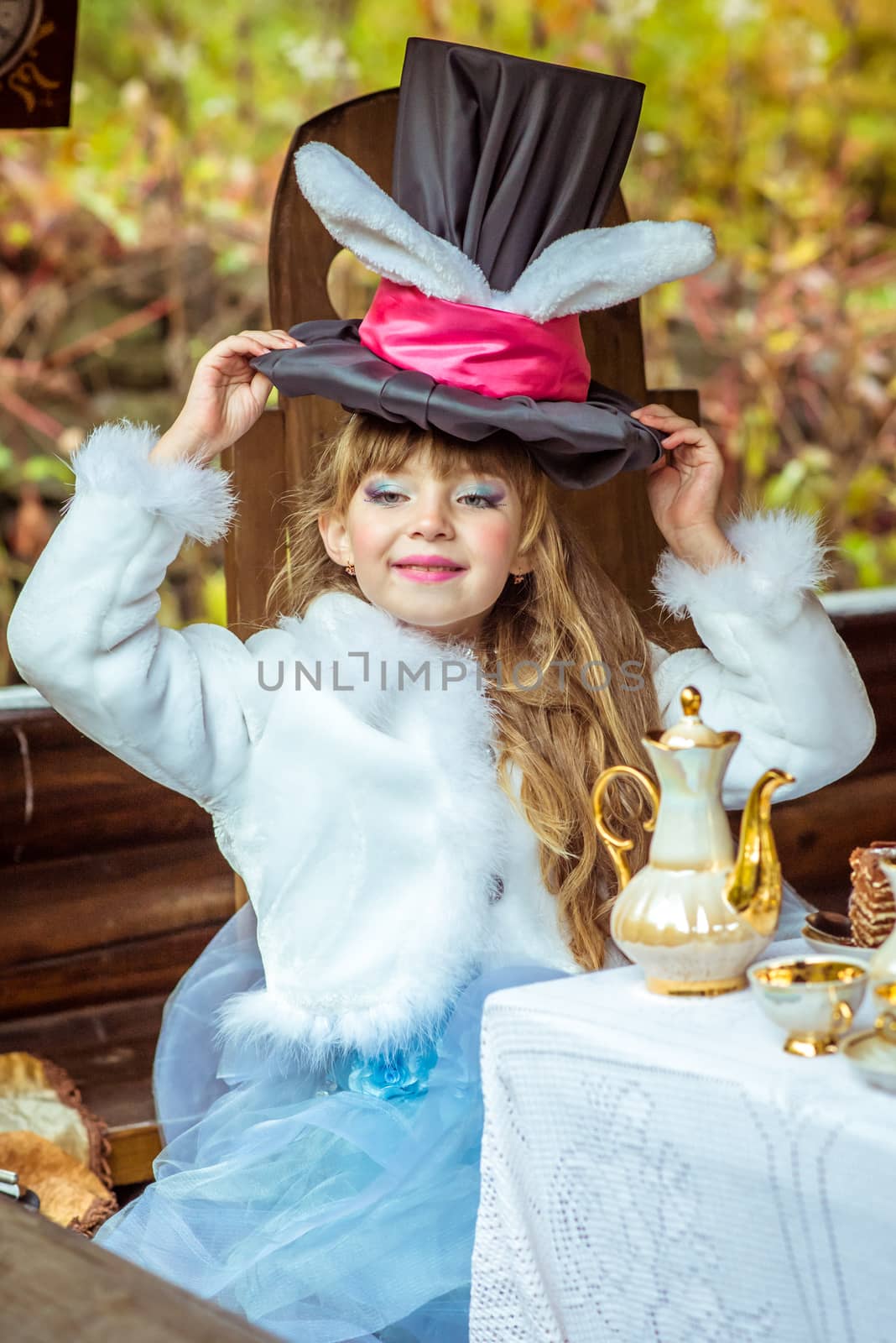 An little beautiful girl holding cylinder hat with ears like a rabbit over head at the table by okskukuruza