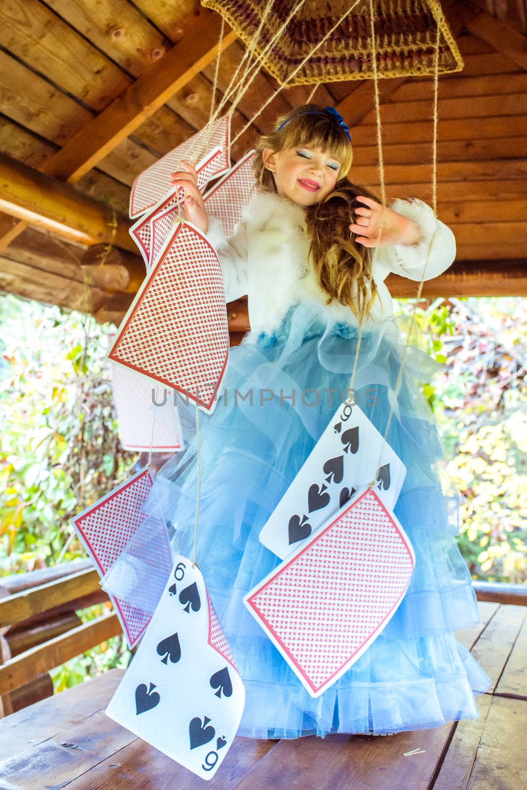 An little beautiful girl playing and dancing with large playing cards on the table by okskukuruza