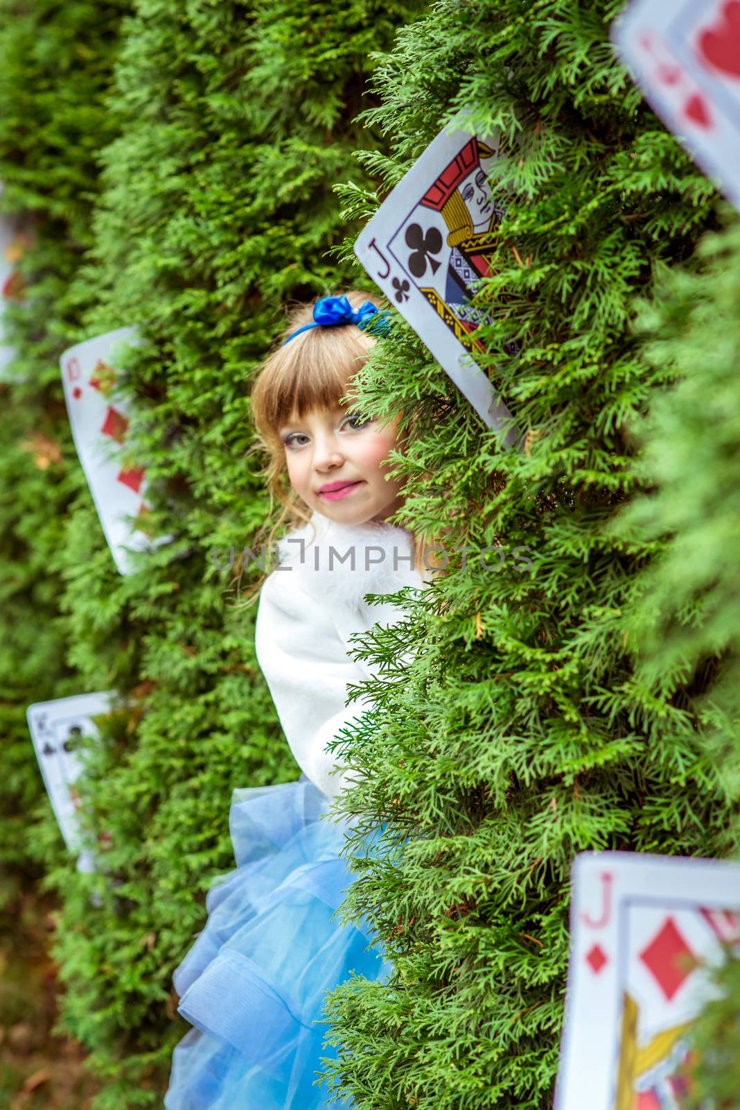 An little beautiful girl in a long blue dress looking from under the fir trees by okskukuruza