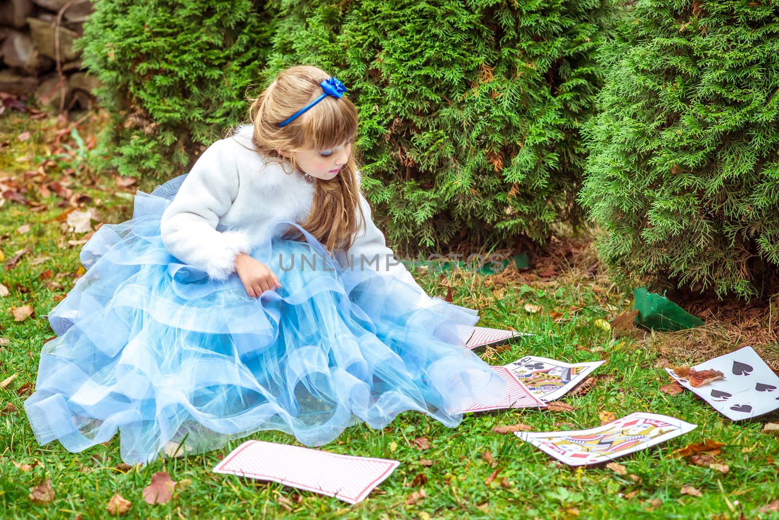 An little beautiful girl in a long blue dress sitting on the grass and playing with large game cards by okskukuruza