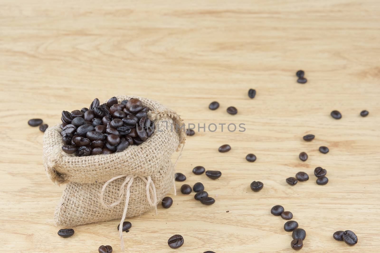 Close up stack of coffee bean in brown sack have coffee bean spread on wooden background.