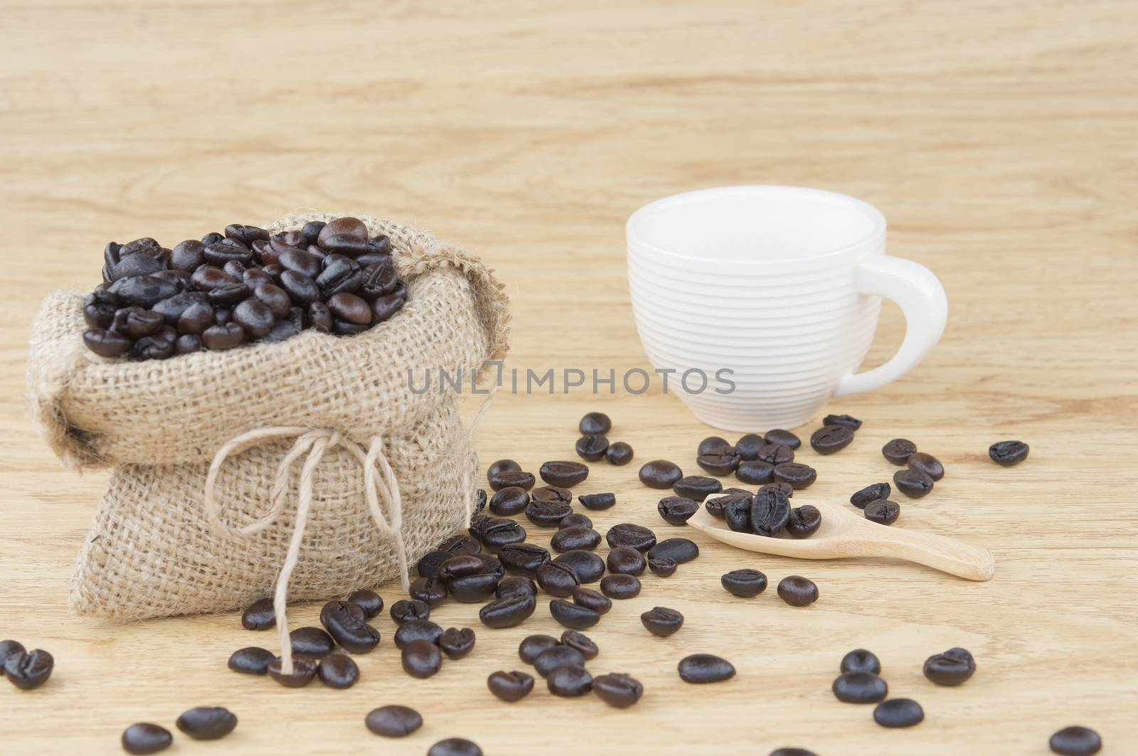 Coffee bean in wooden spoon have blur brown sack of coffee bean and white cup on wooden background.