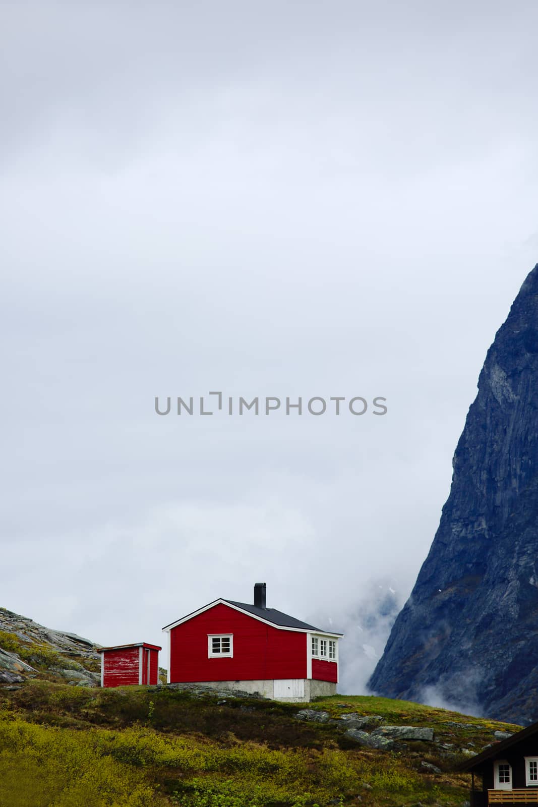 Typical red Norwegian house between high mounatins in summer