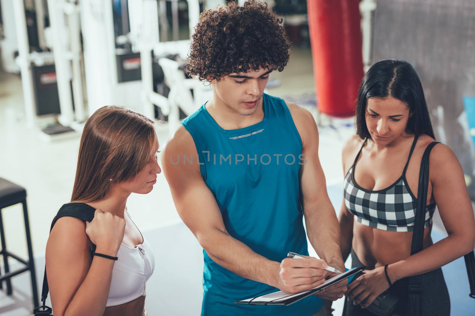 Two happiness female friends consulting with instructor at the gym. 