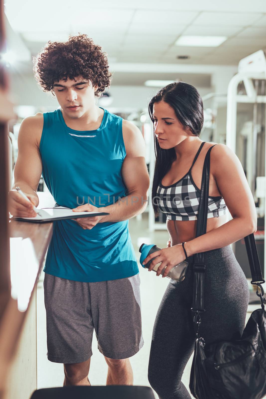 Beautiful young woman consulting with instructor at the gym. 