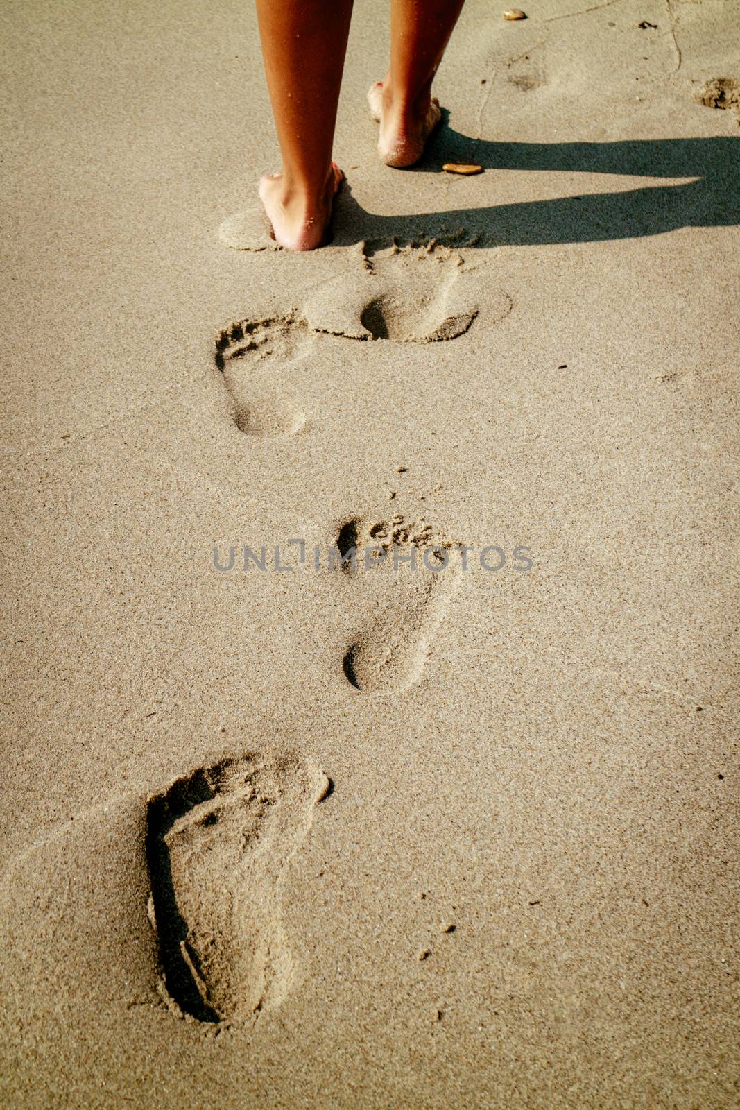 Close-up of a unrecognizable woman legs walking on the beach and leaving footprints in the sand. Rear view.