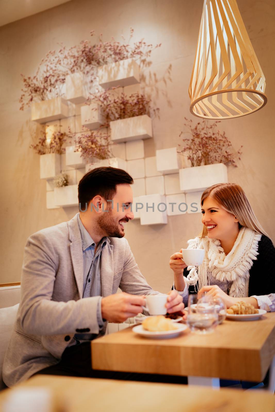 Young man and young woman sitting at cafe and talking with smile. They drinking coffee and having breakfast.