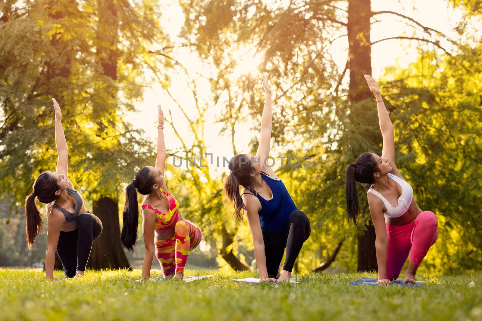 Four beautiful female friends doing yoga in the park. 